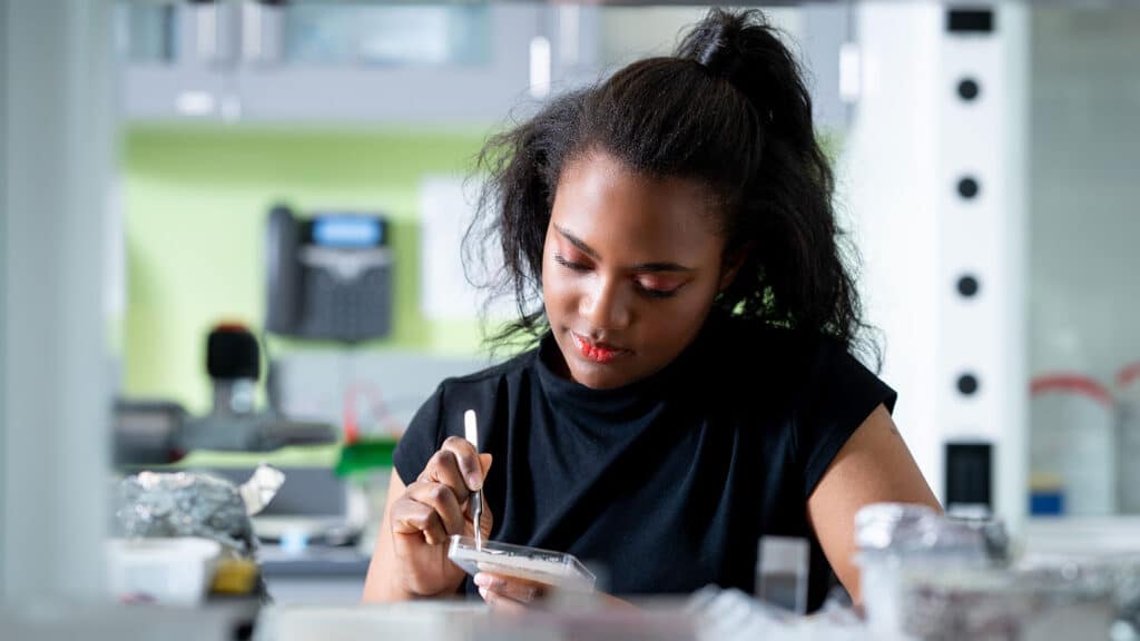 A portrait style shot of a student holding a sharp-bladed research tool and using it to work with a flat object held in her other hand.