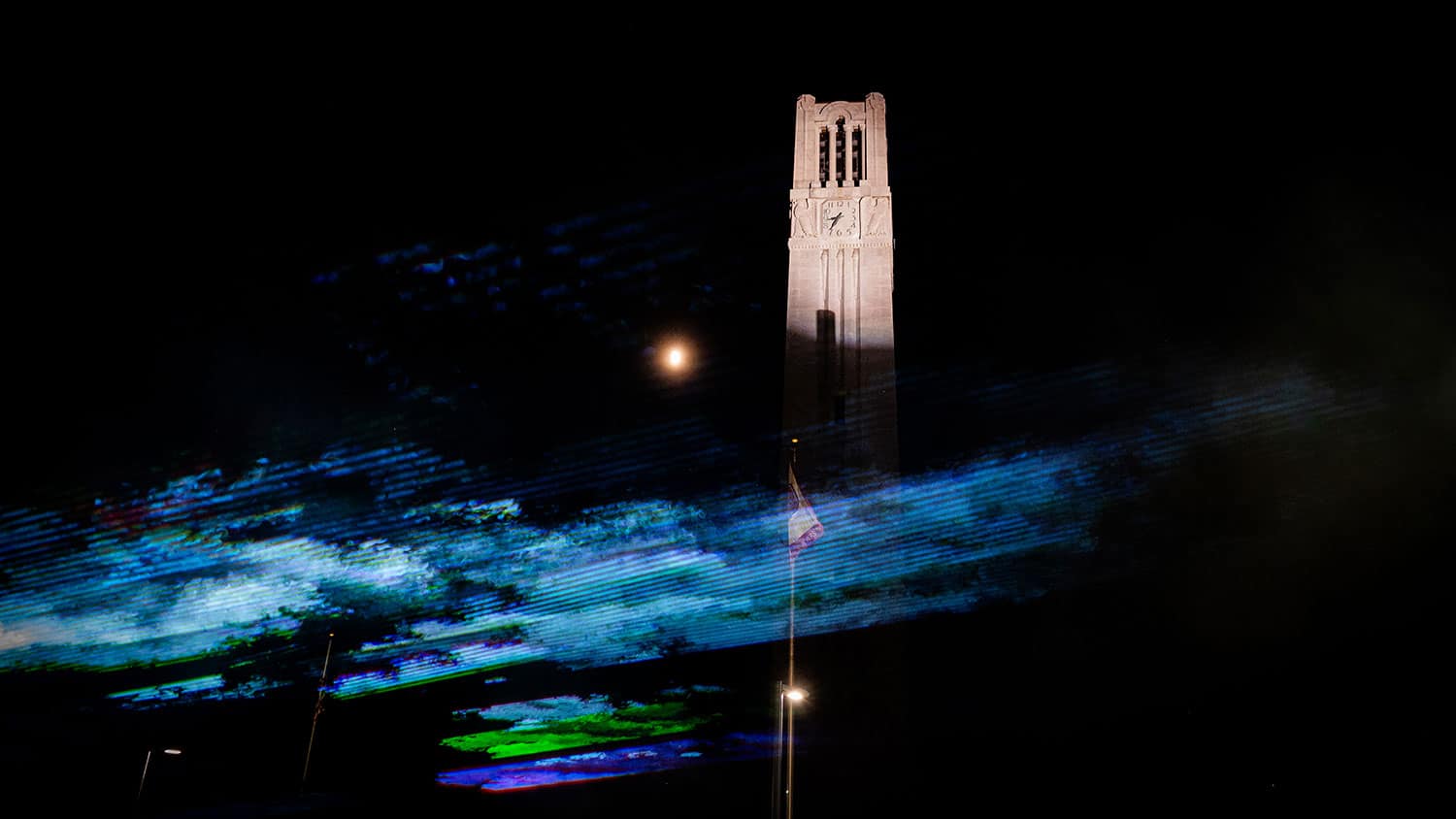 A view of the Belltower at night with blue, green and violet lights flickering across the bottom of the screen in front of the Belltower.