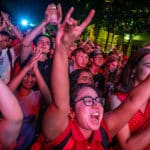 A wide shot of a crowd of NC State students and supporters at nighttime as they hold up the Wolf Ears signal.