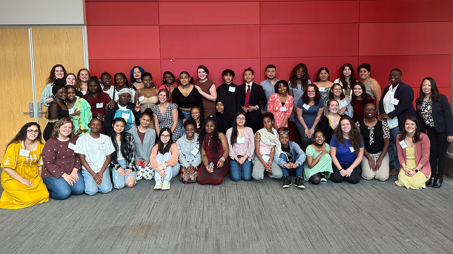 A large group of people who participated in the event in front of a red wall