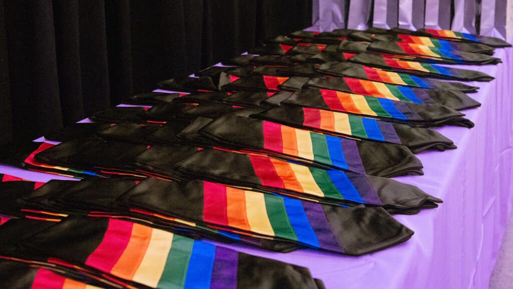 Rainbow graduation stoles are lined up on a display table.