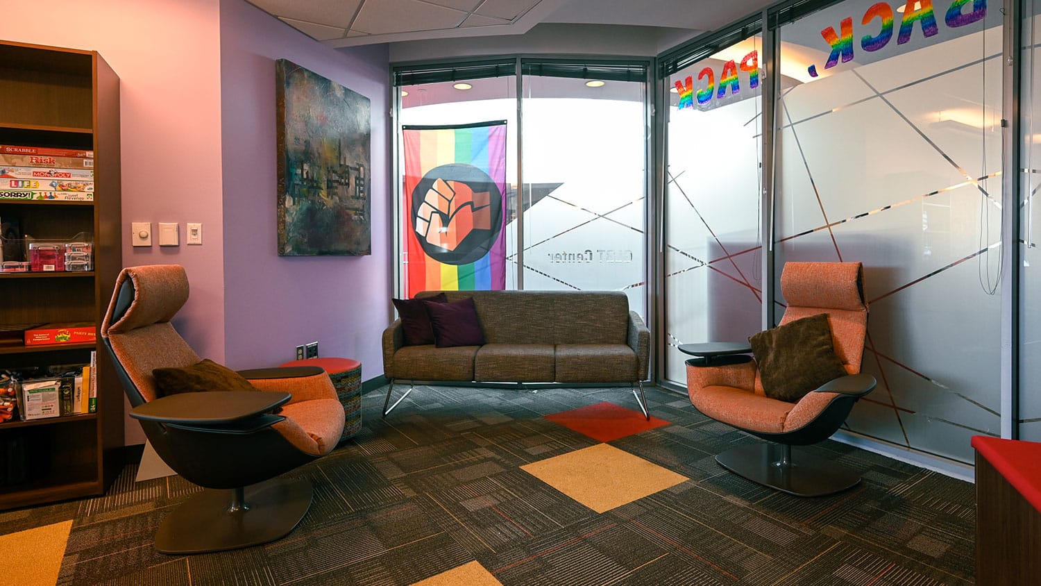 A corner of the LGBTQ Pride Center featuring a couch and two cushioned seats with attached adjustable desktops.