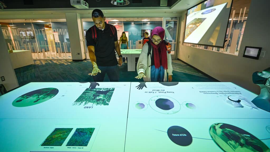 Two people stand looking down at a table featuring a digital visualization.