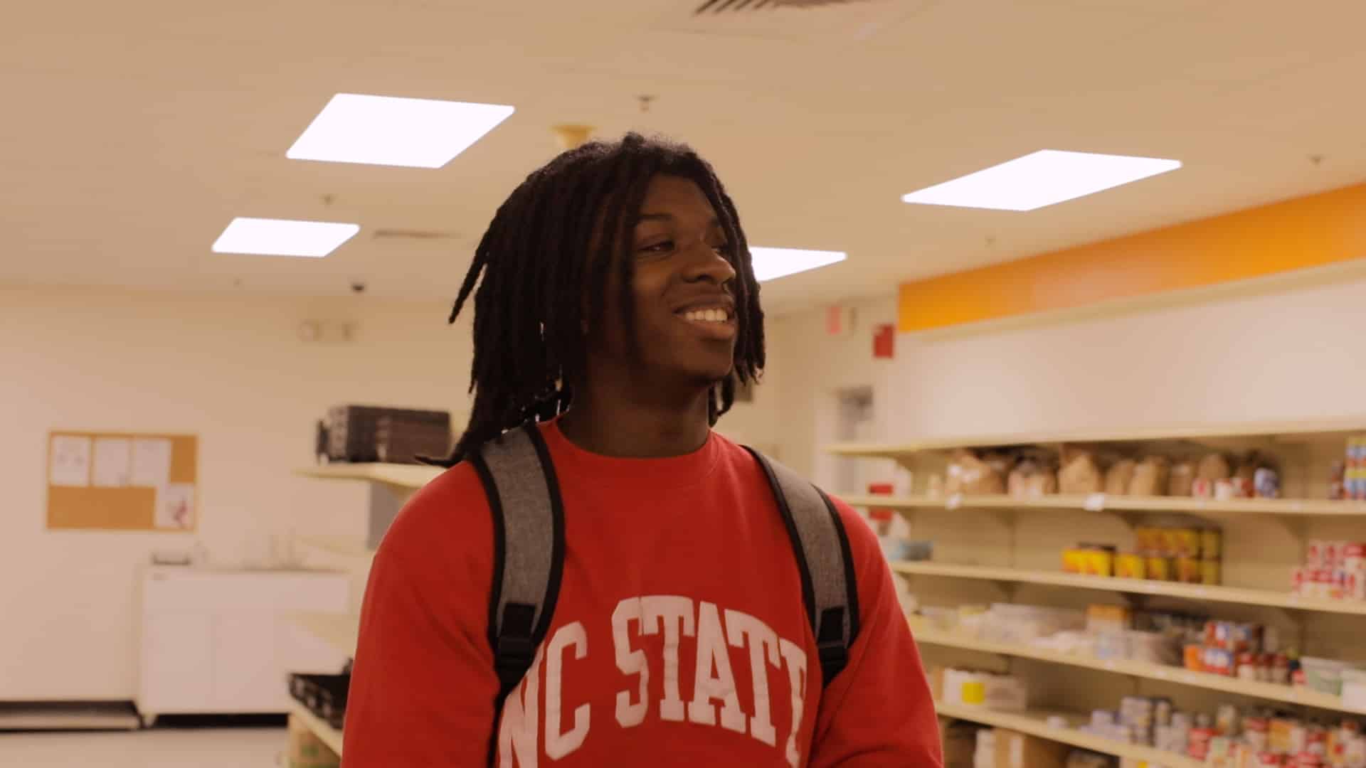 An NC State student smiles as he walks down the aisle of the Feed the Pack Food Pantry. 