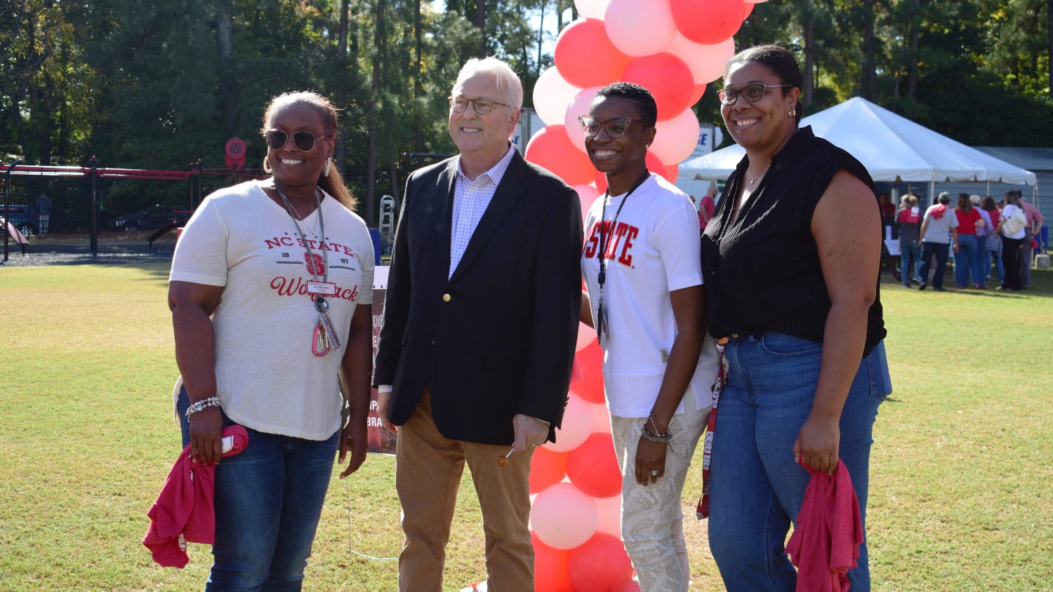 Three employees pose for a photo with Chancellor Woodson in front of an outdoor balloon arch.