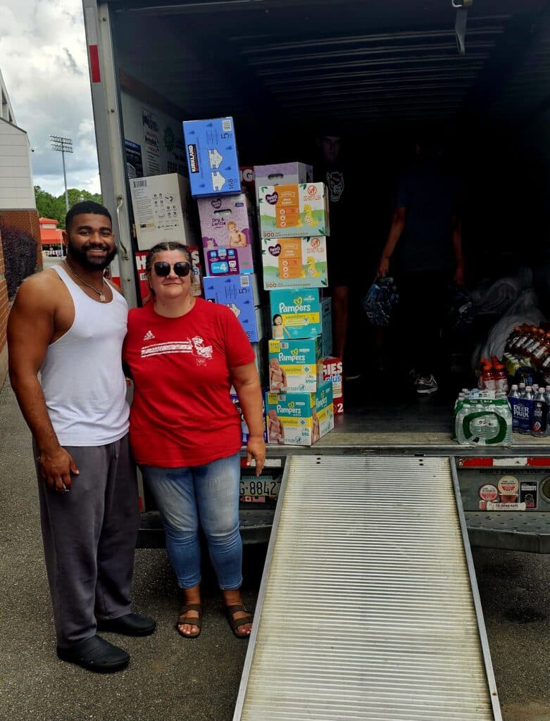 Davin Vann posing with an NC State football fan in front of a truck loaded with supplies