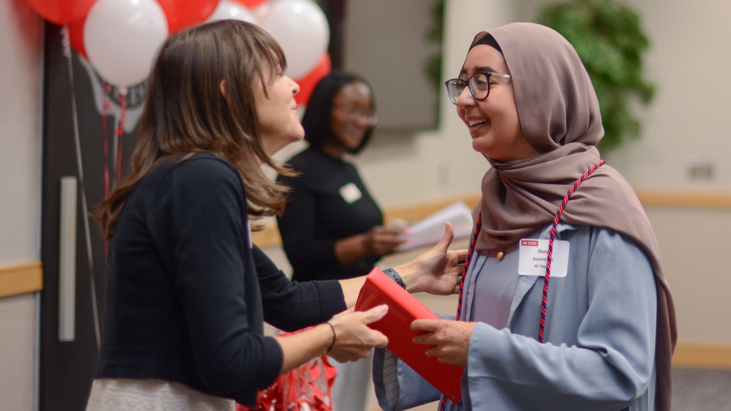 A staff member congratulates a student and hands her a gift.