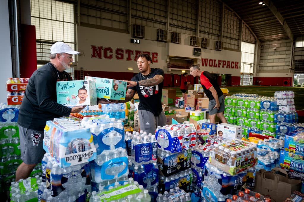 Football coaches and athletes load supplies from the team's practice facility