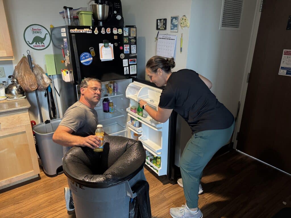 Two staff discard expired items from a refrigerator at UNC Asheville