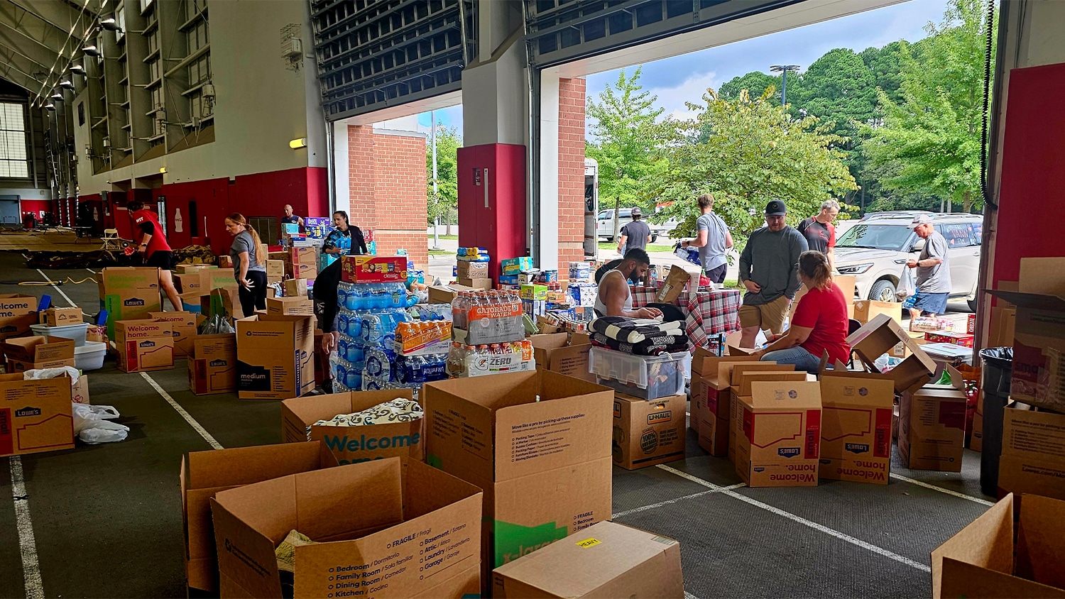 Staff and community members load boxes of supplies at the NC State football team's practice facility