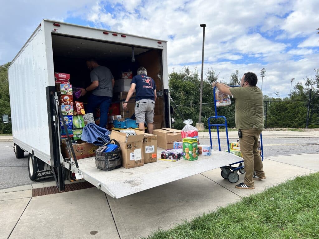 Three people unload non-perishable foods and other goods from the back of a truck at UNC Asheville