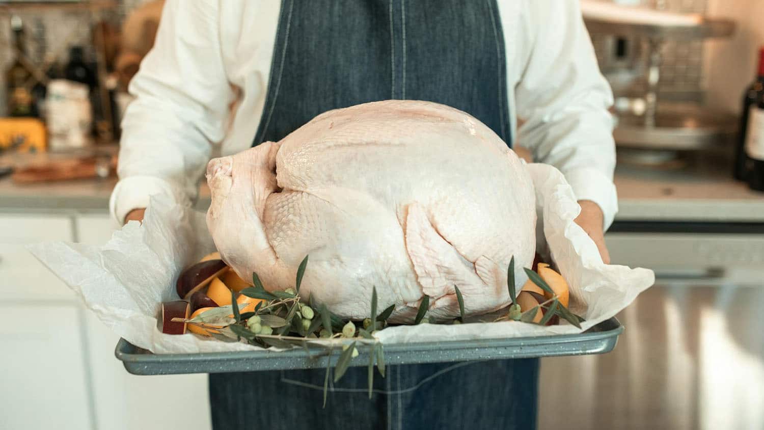 a cook is holding an uncooked turkey on a roasting pan. i hope the cook took steps to reduce the risk of foodborne illness