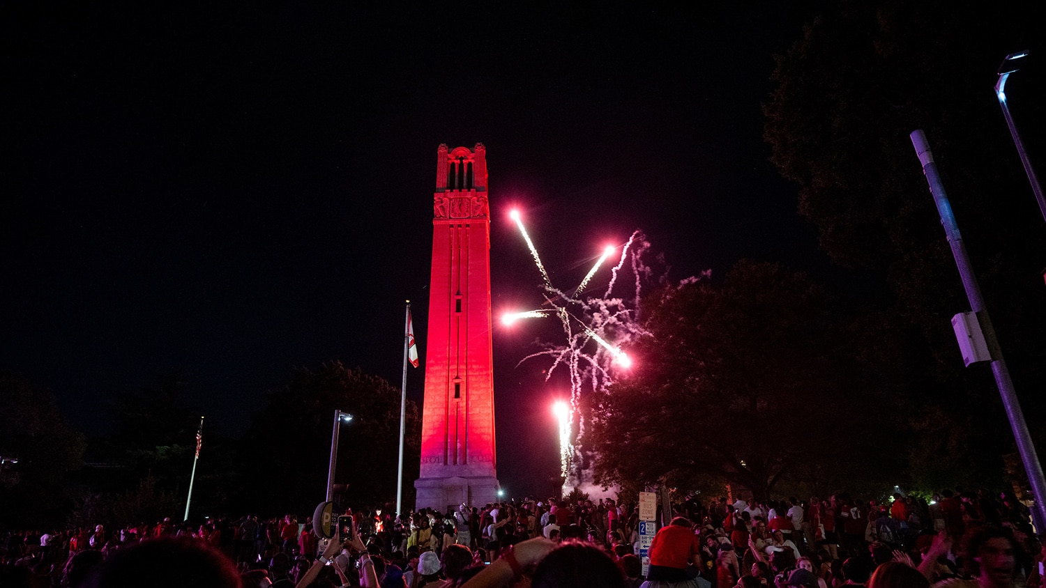 The NC State belltower lit red with fireworks in the night sky behind it at the 2024 Packapalooza event.