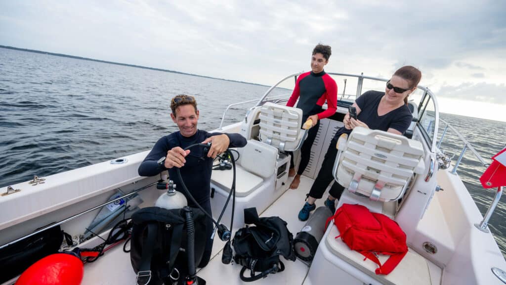 Tal Ben-Horin prepares his scuba diving gear as Astrid Schnetzer and Zakir Bulmer look on.