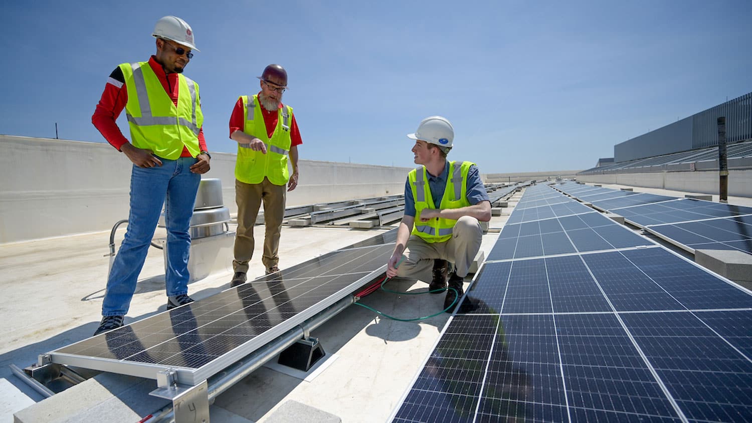 Three people take a look at solar panels installed on the Fitts-Woolard Engineering building on Centennial Campus.