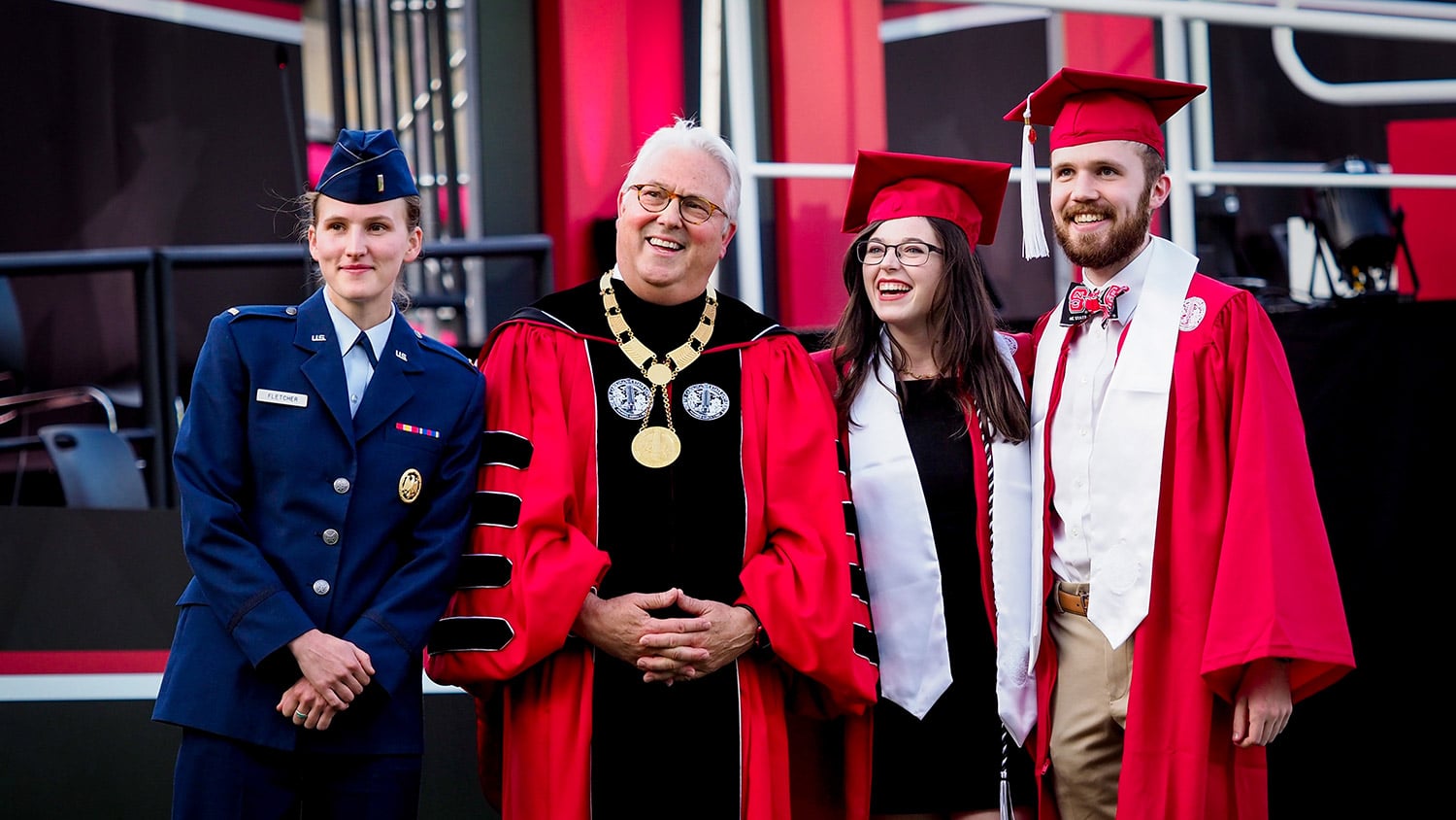 Chancellor Woodson and three students pose for a photo wearing graduation and ROTC attire.