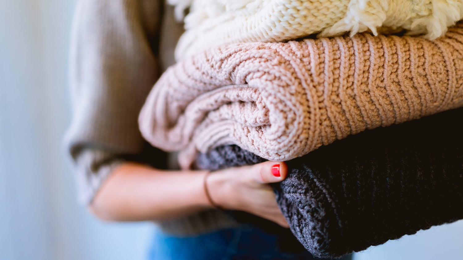 A person carries a stack of winter sweaters