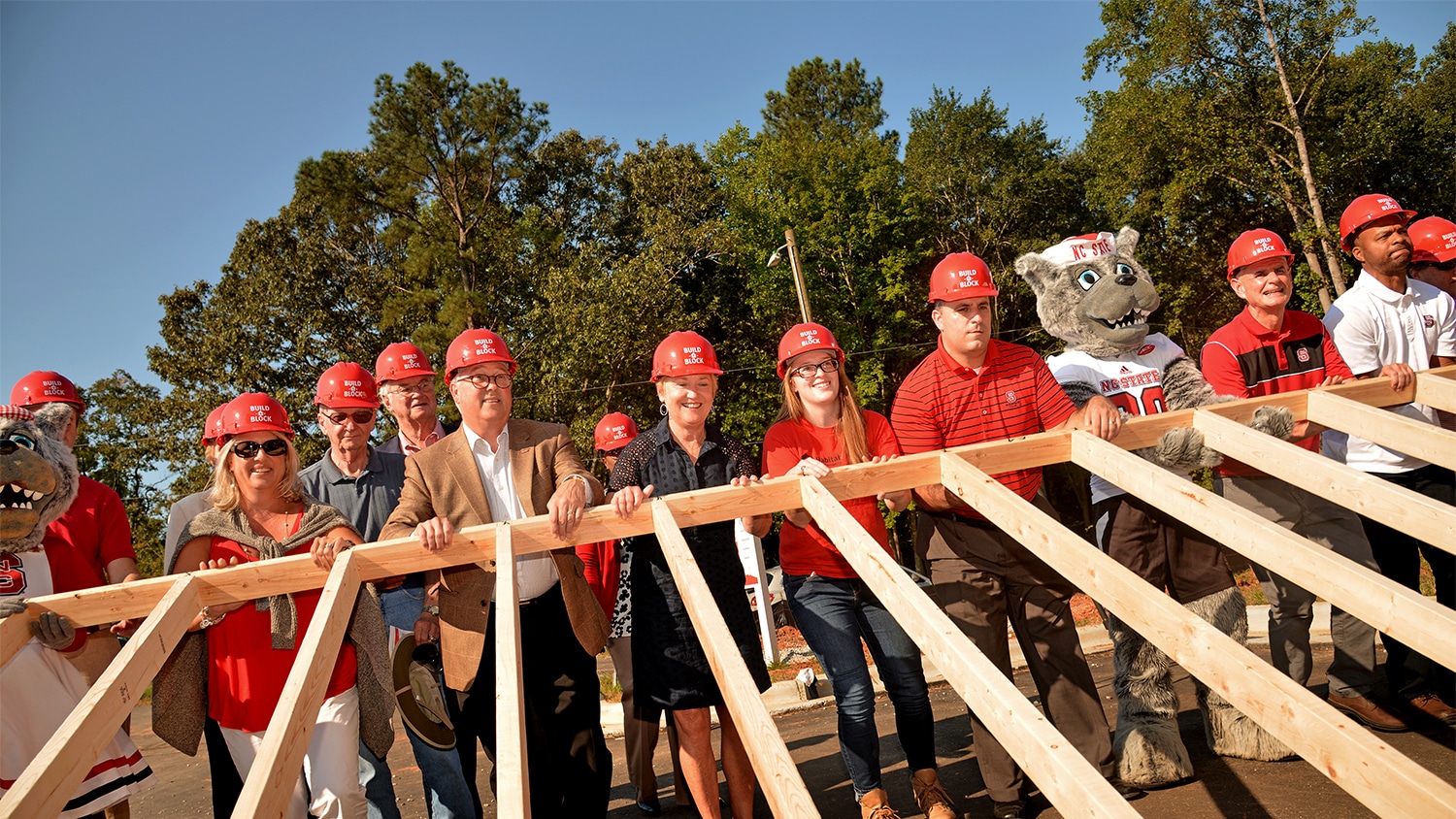 Chancellor Woodson and a group of people in hard hats raise a framed wall together.