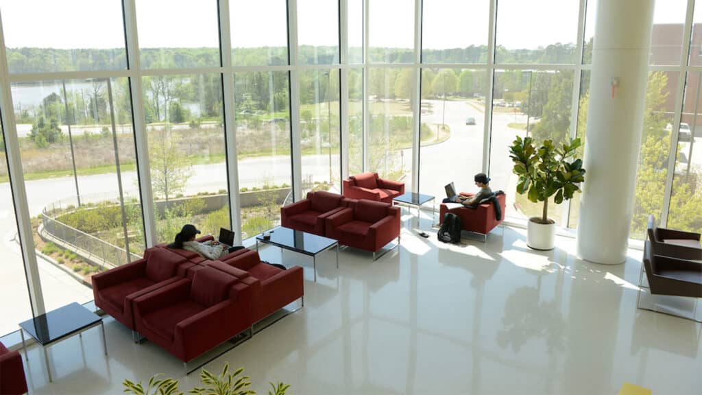 Students sit on couches and chairs while working on laptops in a naturally-lit open area of Hunt Library