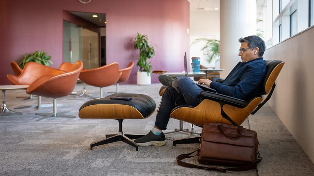 A member of the campus community sits in a comfortable chair and works on a laptop in a common area of Hunt Library