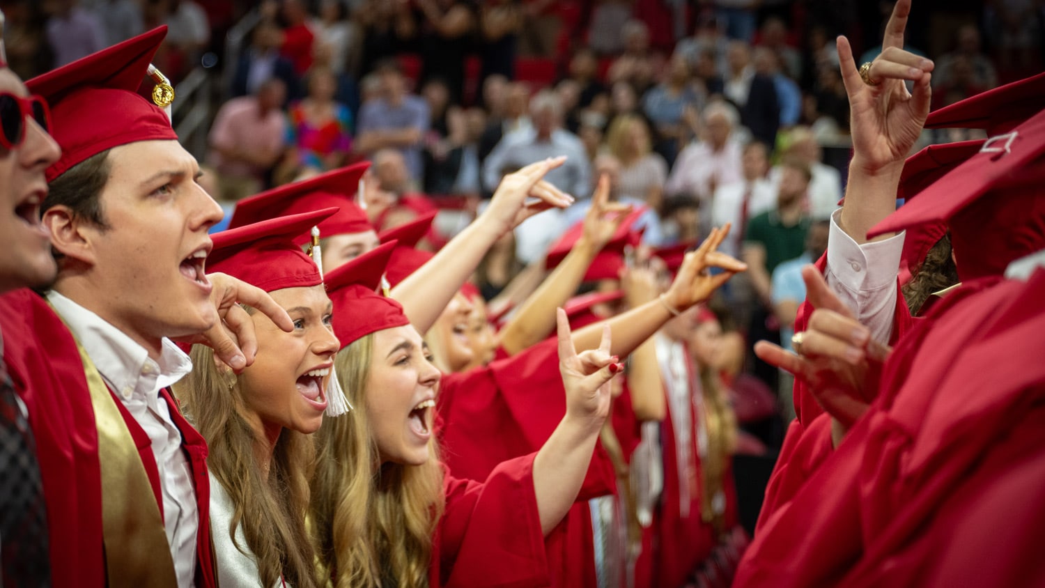 Graduates make wolfie hand symbols at a commencement ceremony