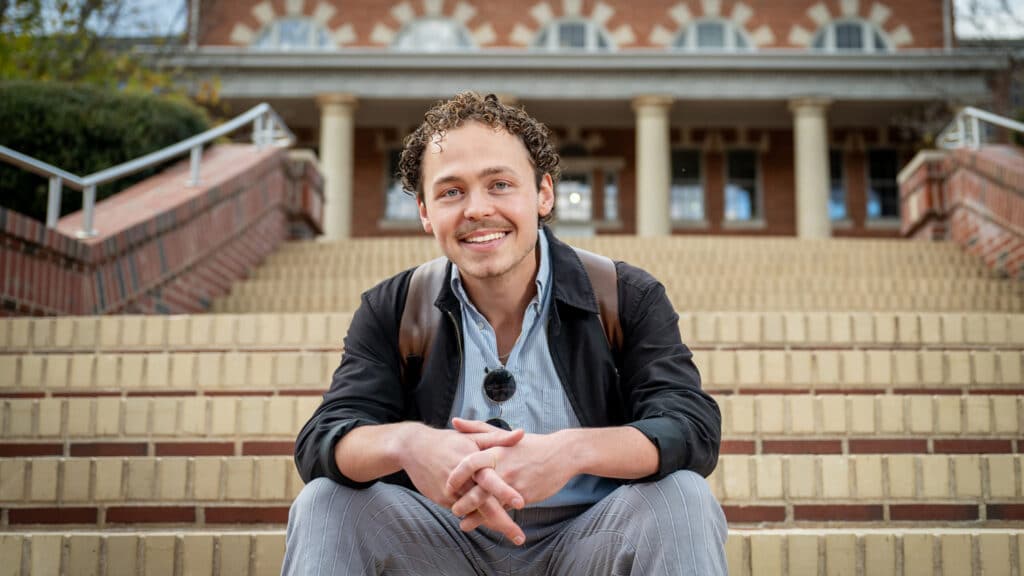 Elliott Gyll sitting on the steps in front of the 1911 Building on NC State's campus