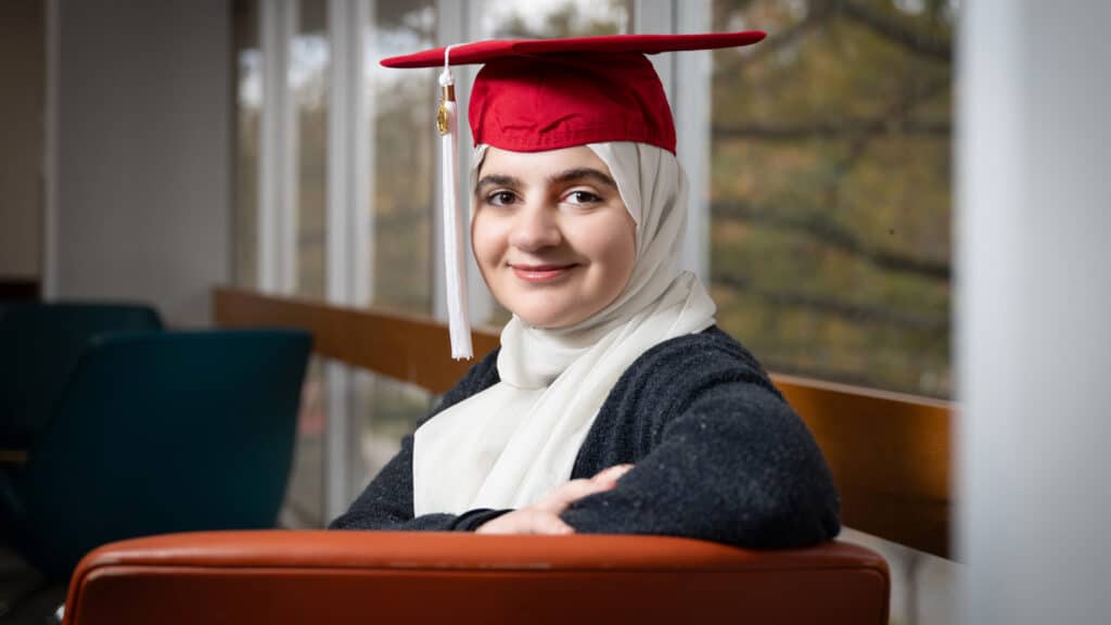 Sarah Salahat smiles at the camera, wearing her red graduation cap