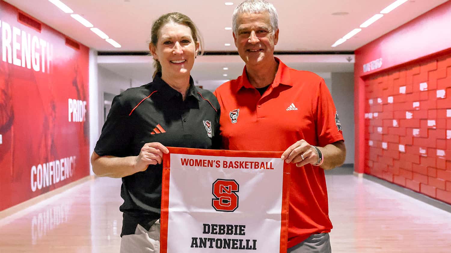 Athletic director Boo Corrigan presents Debbie Antonelli with a banner that will be displayed in the Ring of Honor at Reynolds Coliseum.