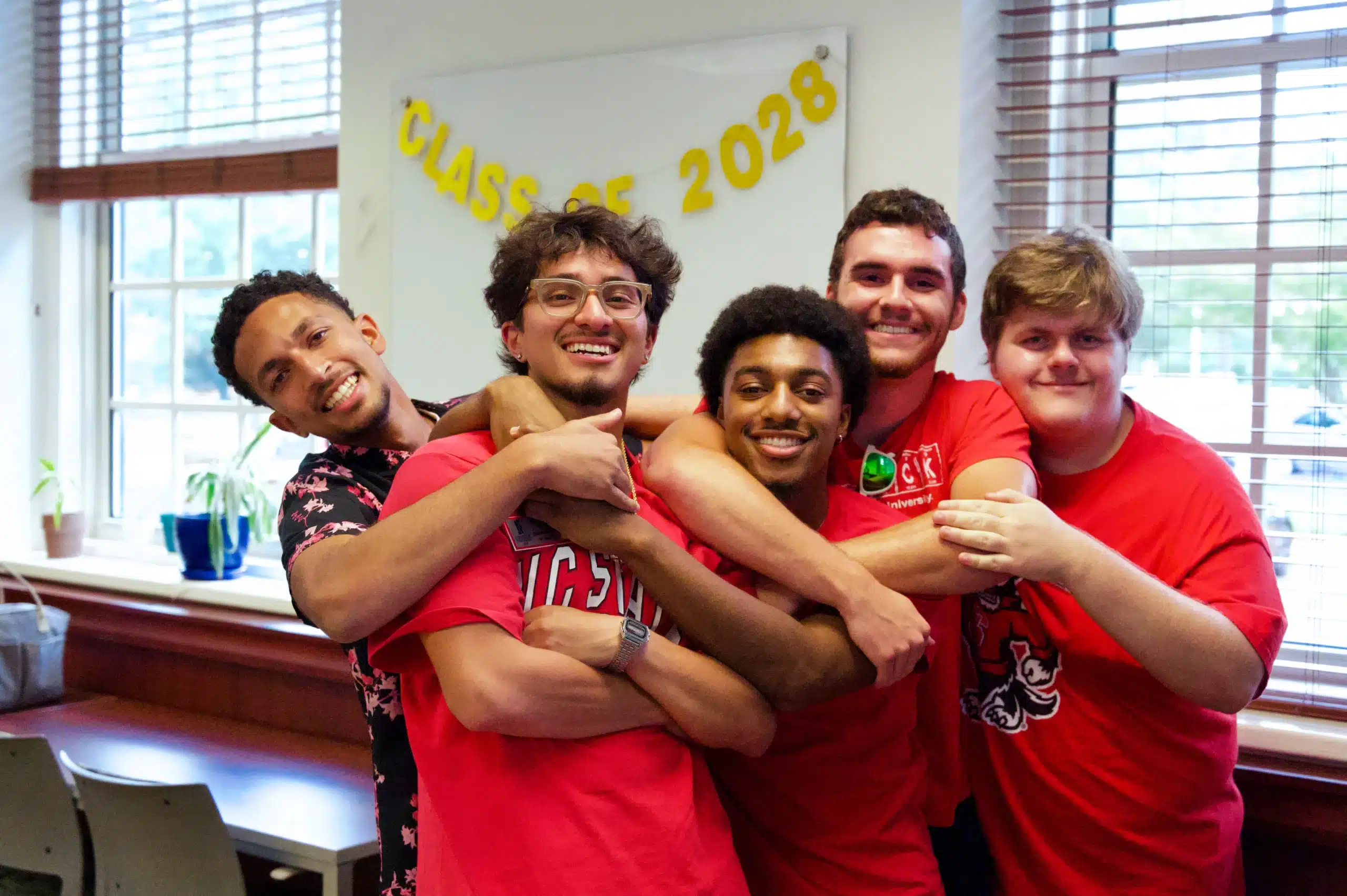 Five students pose with their arms around each other and smiling.