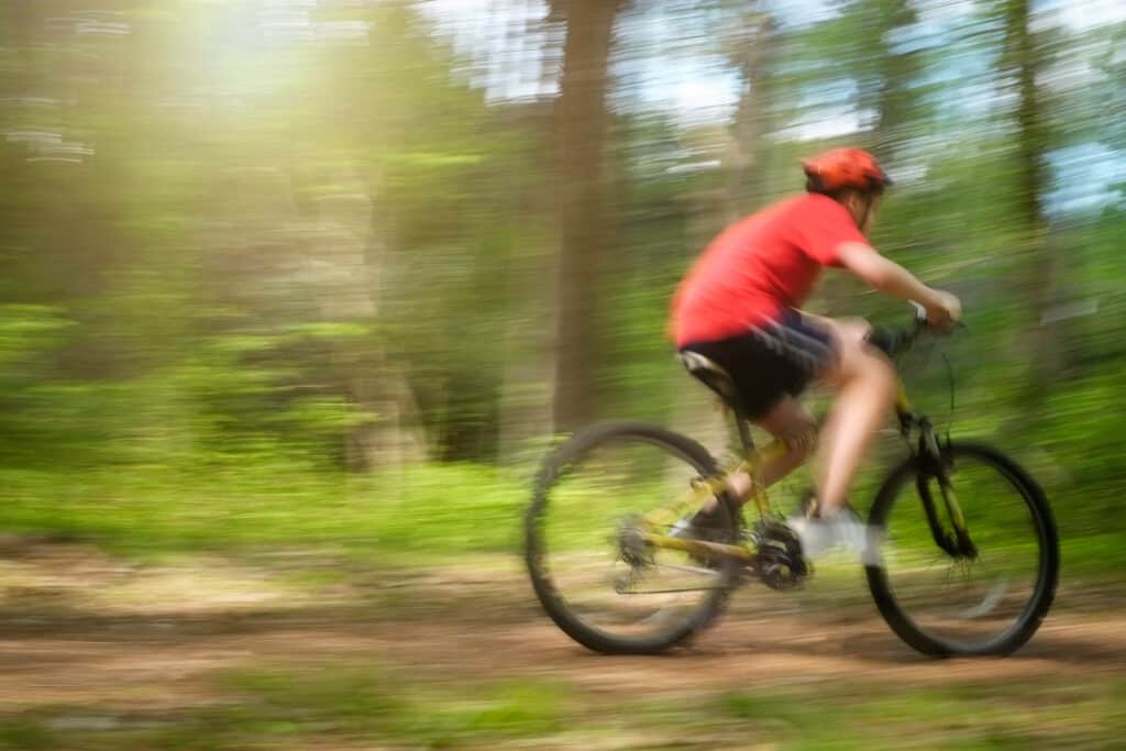 A biker in a red helmet, red shirt and black gym shorts rides a bike through a trail in Lake Raleigh Woods.