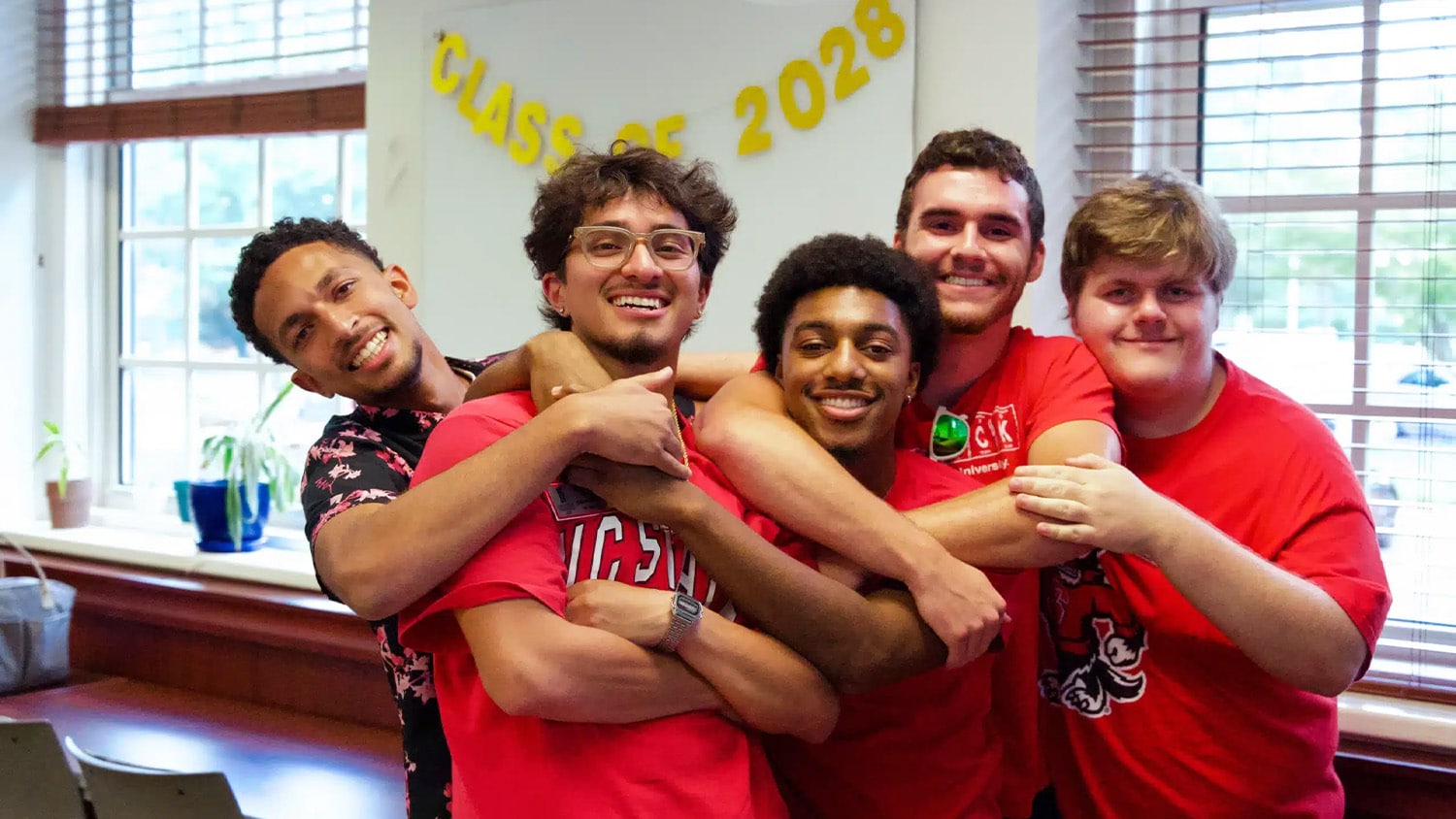 Five students pose with their arms around each other and smiling.