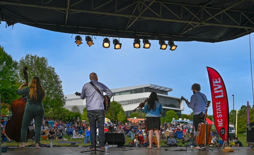 A bluegrass band faces the audience and performs on a stage on Centennial Campus for LIVE at Lake Raleigh. 