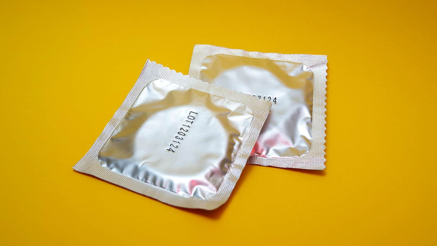 two condoms in foil wrappers rest on a yellow background