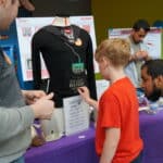 Textiles students Ethan Hill and Faisal Abedin show a child how to play musical notes on their smart clothing display