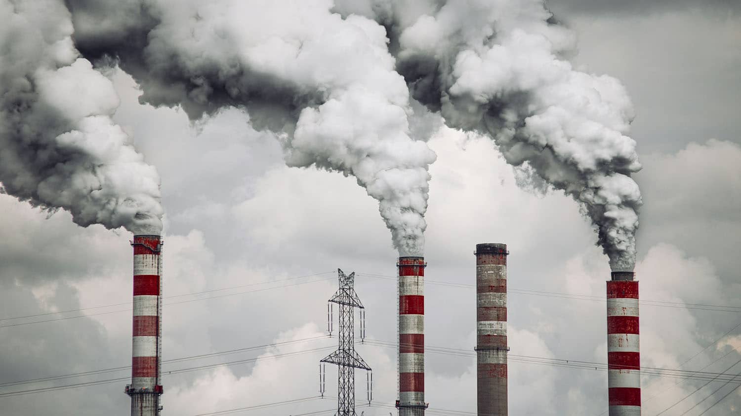 four industrial smokestacks are belching huge clouds of smoke, silhouetted against the skyline