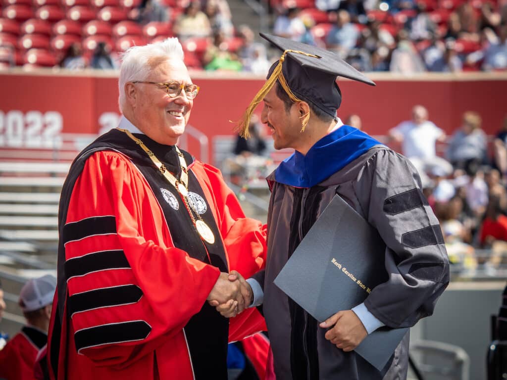 Woodson shakes hands with a graduate on stage during commencement.