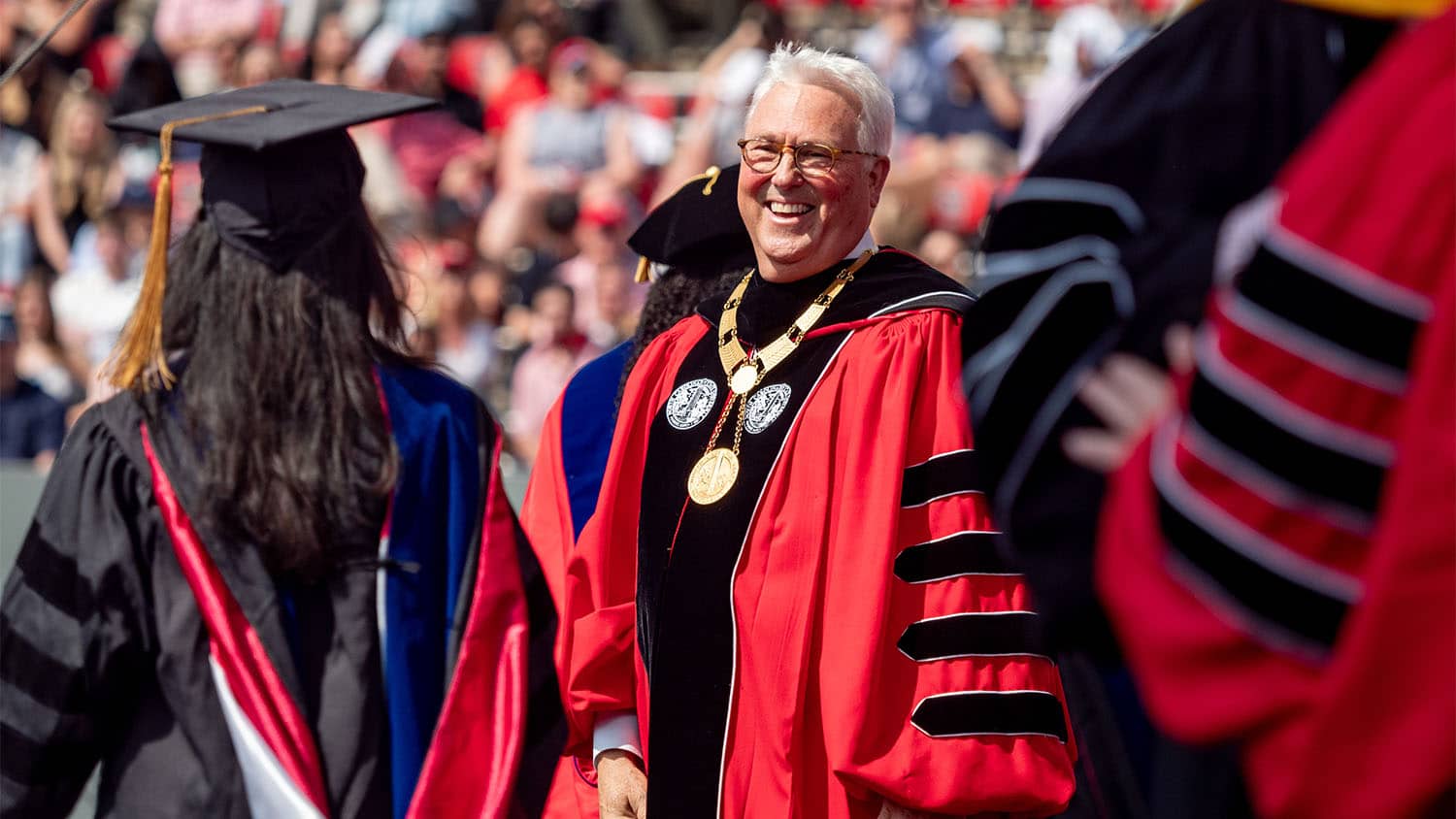 Randy Woodson smiles and greets 2025 graduates as they enter Carter-Finley Stadium.
