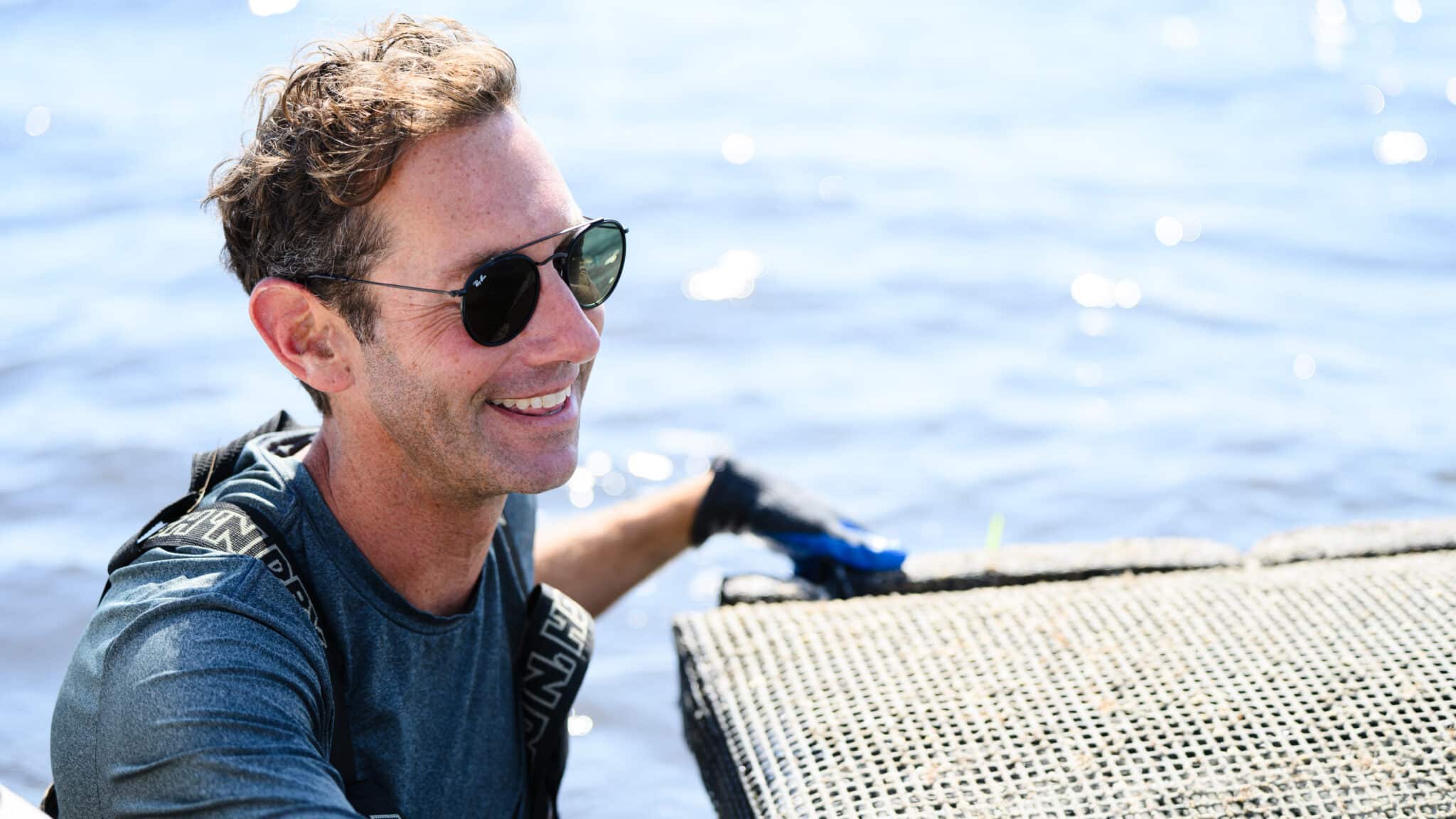Assistant professor Tal Ben-Horin stands next to an oyster bag near ocean water.