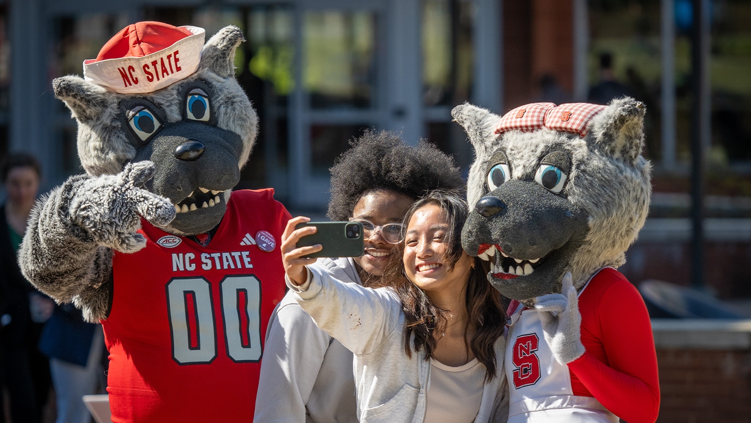 Two students take a selfie with Mr. and Ms. Wuf in front of Talley Student Union.