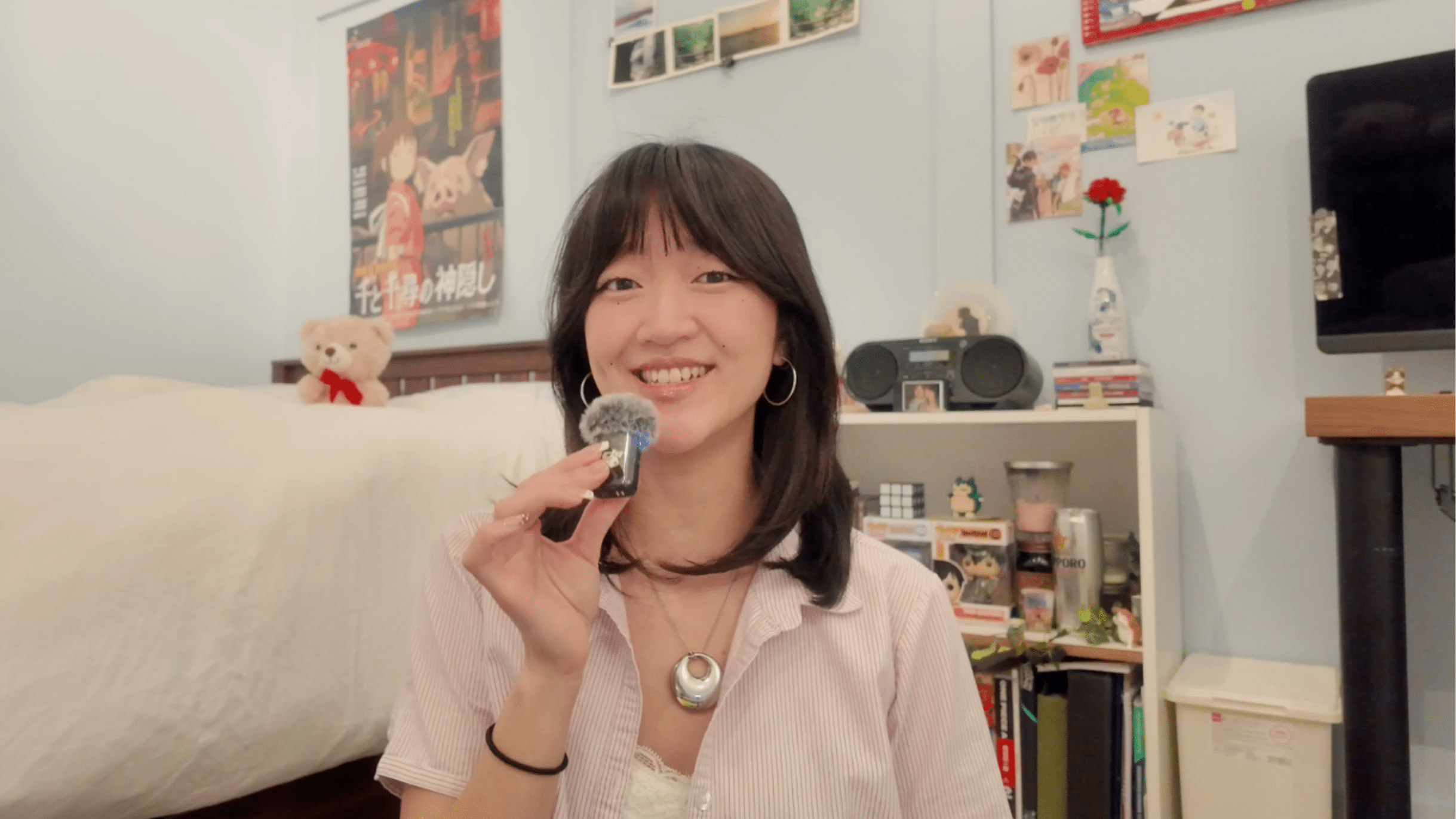 Student Lia Han holding a bluetooth mic while talking to the camera from her room.