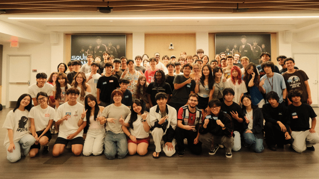 A large group of students pose inside a studio with Squid Games posters in the background.