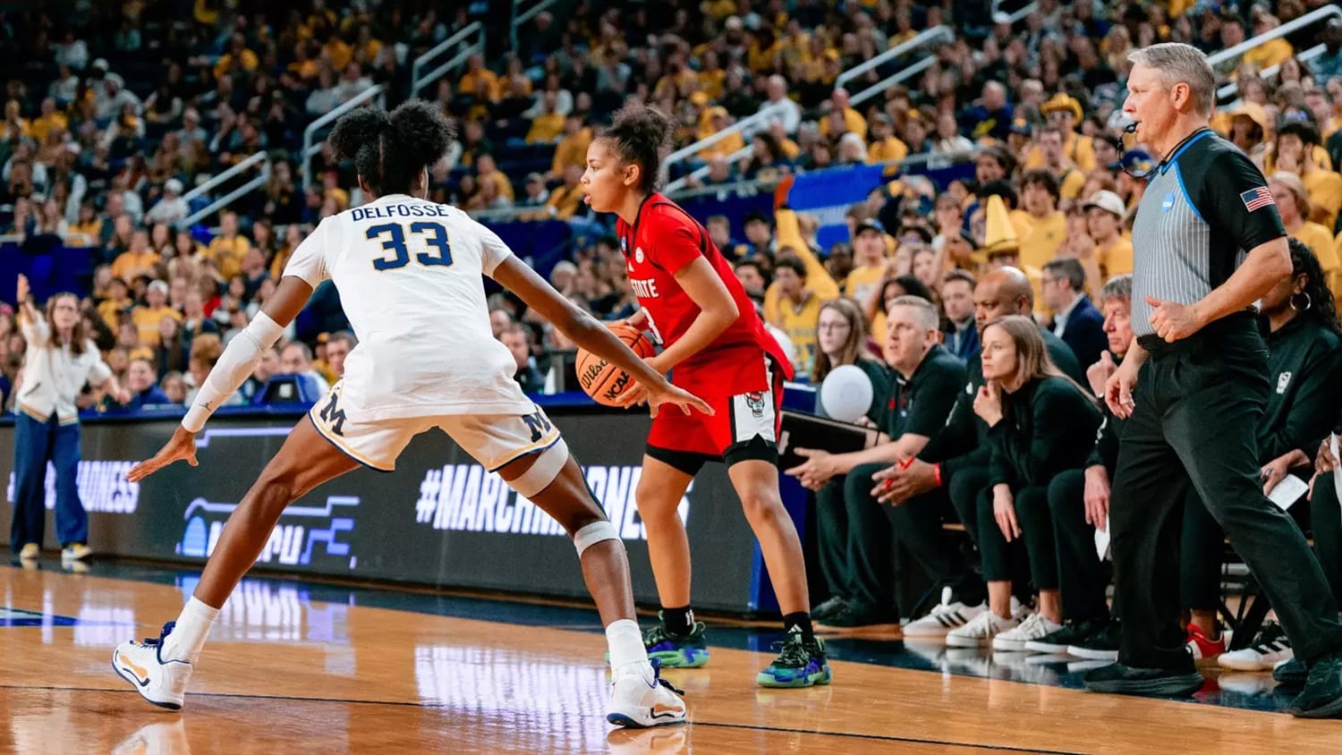 A member of the women's basketball team looks to pass the ball while an opposing player guards her.